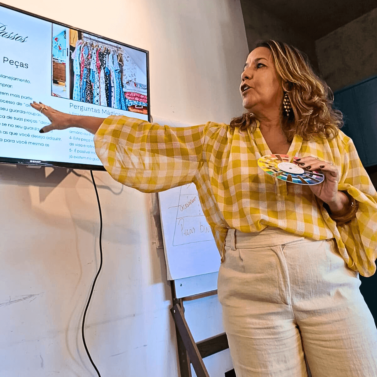Consultora de Imagem Lili Machado ministrando palestra sobre coloração pessoal e estilo, segurando um círculo cromático e explicando combinações de roupas em apresentação no Rio de Janeiro.