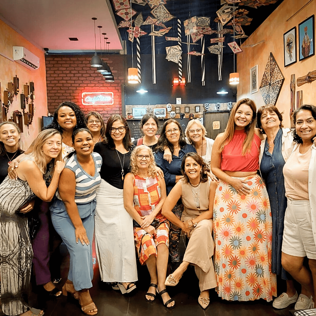 Grupo de mulheres posando para uma foto em uma sala com paredes decoradas.