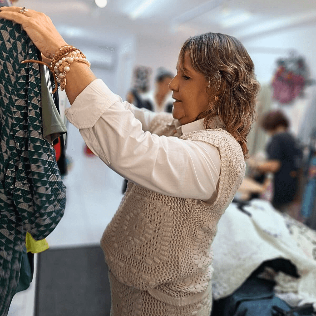 Lili Machado sorrindo e segurando uma peça de roupa, provavelmente em um closet ou loja.